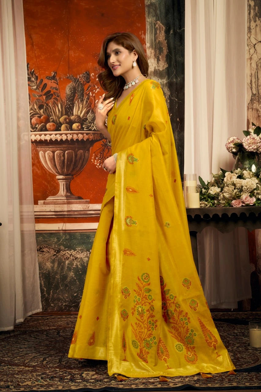 Woman in a yellow saree with floral patterns standing in an elegant room.