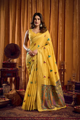Woman in a yellow saree with butterfly patterns standing against an orange curtain.