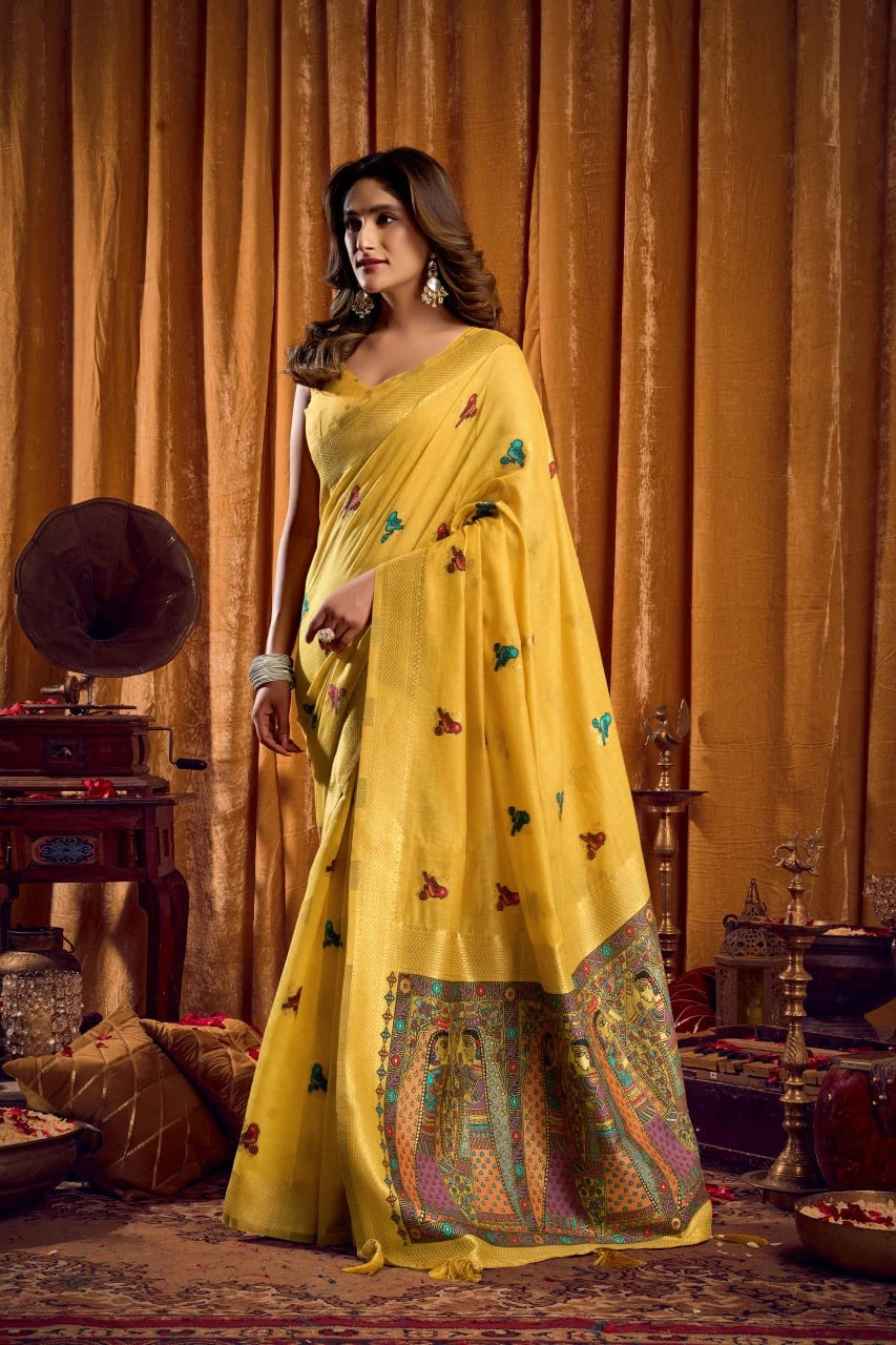 Woman in a yellow saree with intricate patterns standing in a vintage room.