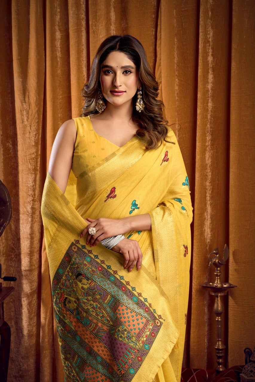 Woman wearing a yellow saree with a patterned border against an orange curtain background