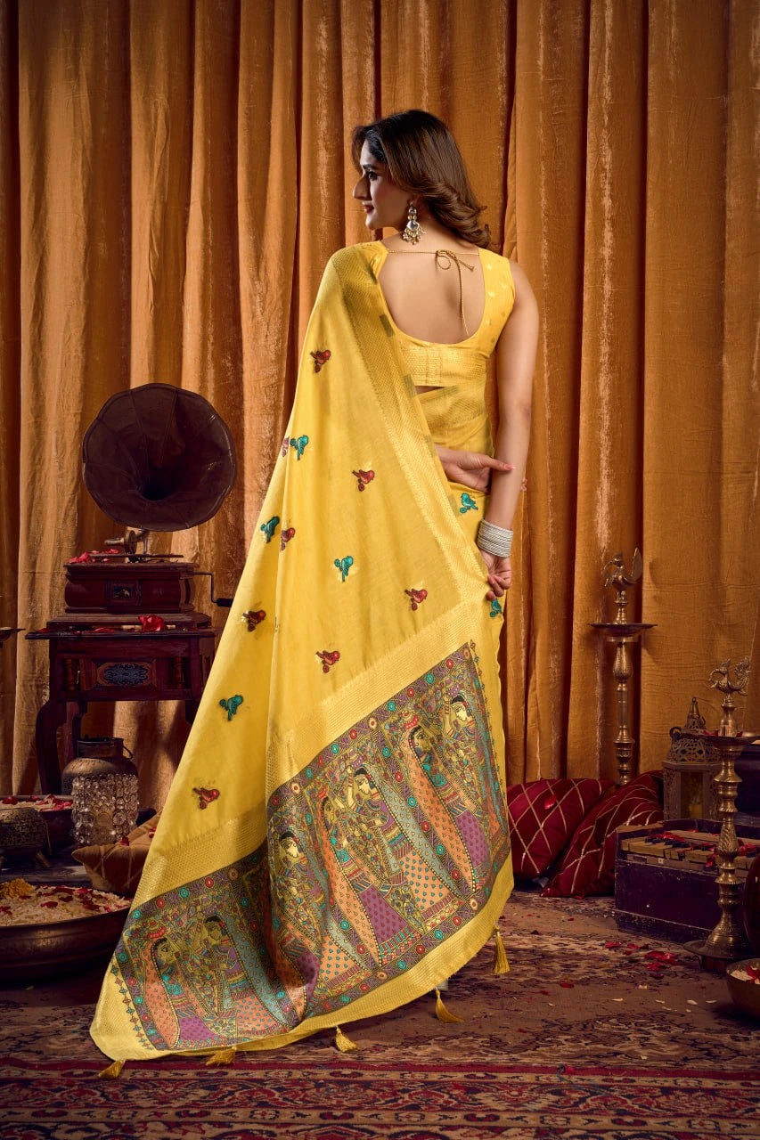 Woman in a yellow saree with intricate patterns standing in a room with vintage decor.