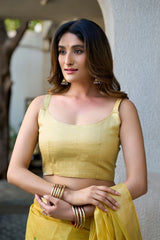 Woman wearing a yellow traditional outfit with gold jewelry against a neutral background