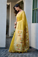 Woman in a yellow saree with floral patterns standing outdoors.