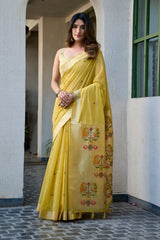 Woman wearing a yellow saree with floral patterns standing against a light-colored wall.