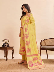 Woman in a yellow printed ethnic suit with pink detailing, posing sideways with a flowing dupatta featuring traditional motifs and borders, paired with flats in a warm-toned indoor setup.