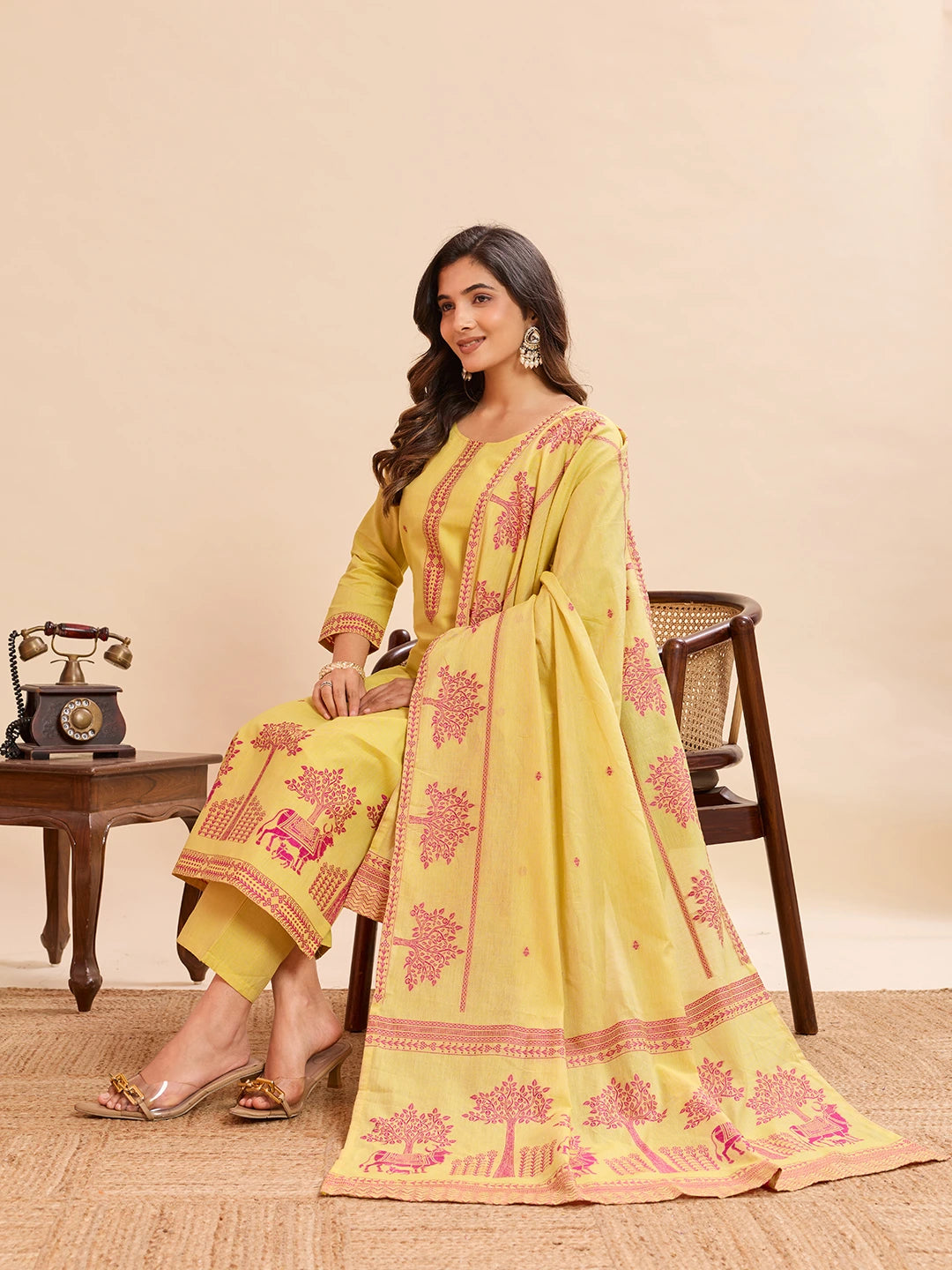 Woman wearing a yellow and pink embroidered traditional outfit in a room setting.