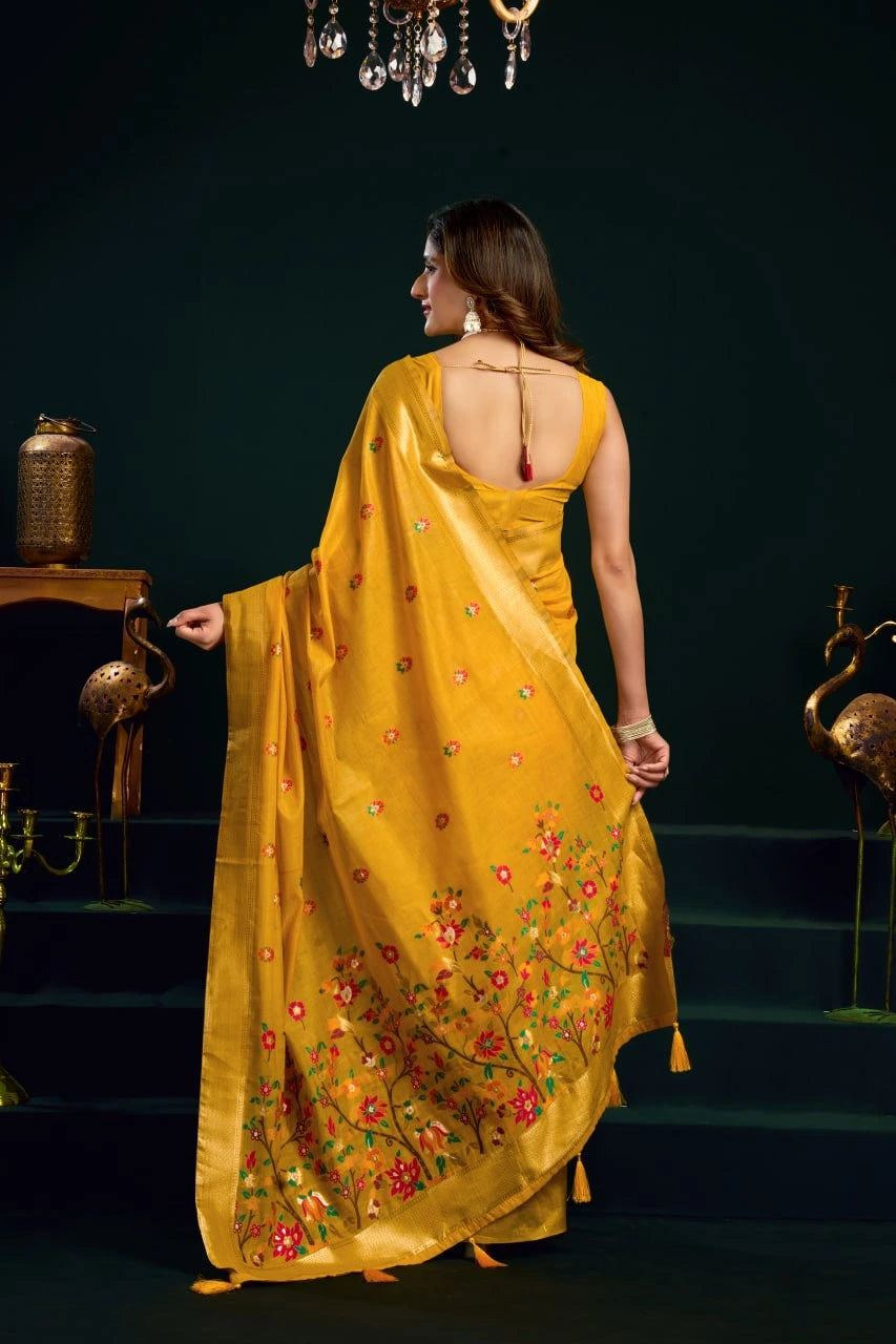 Woman in a yellow saree with floral patterns standing on a dark staircase.