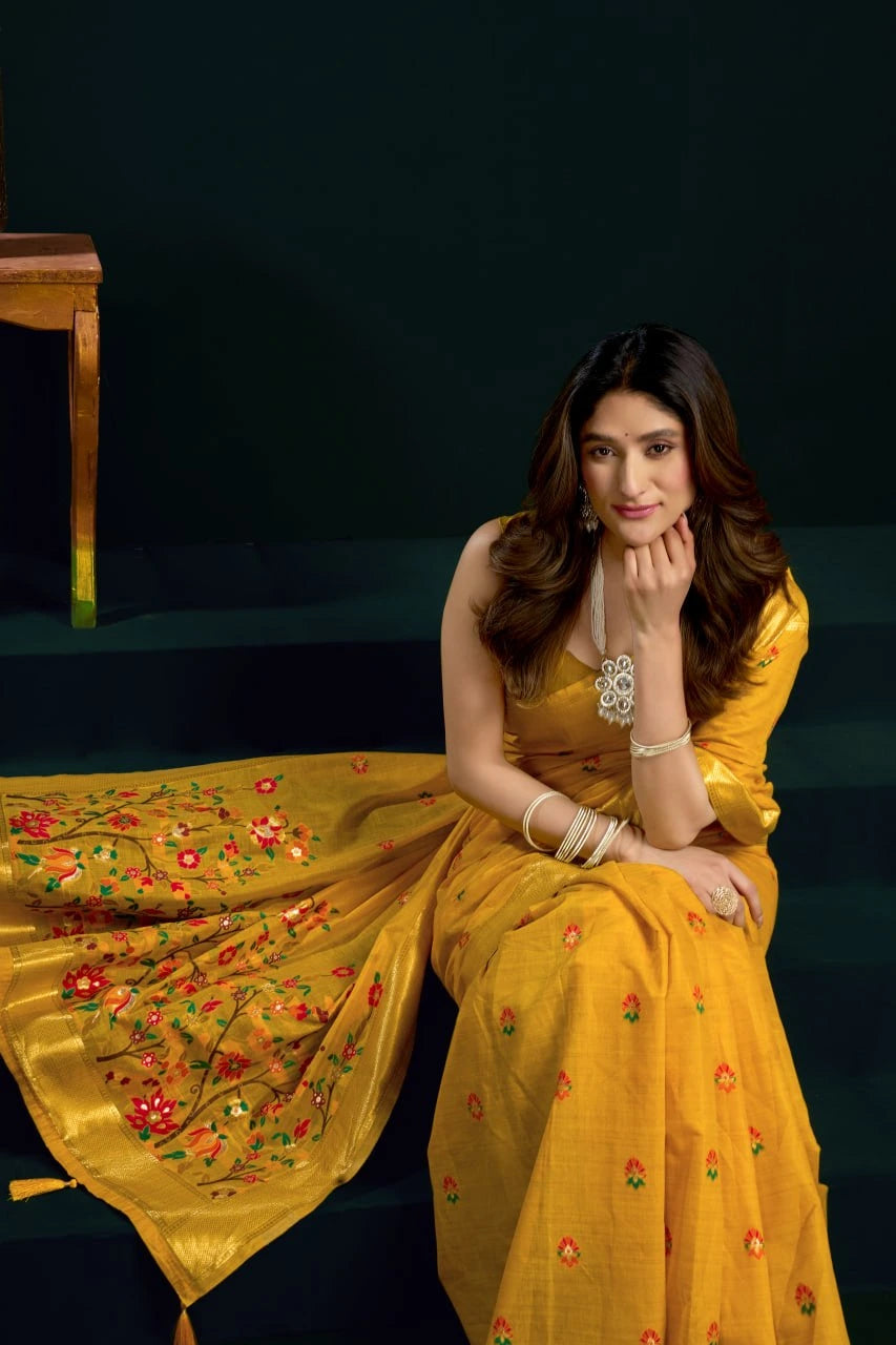 Woman in a yellow saree with floral patterns sitting on a dark background