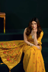 Woman in a yellow saree with floral patterns sitting on a dark background
