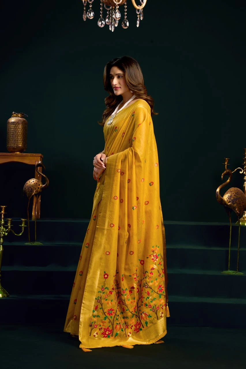 Woman in a yellow saree with floral patterns standing on a dark staircase.