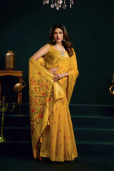 Woman in a yellow saree with floral patterns standing against a dark background