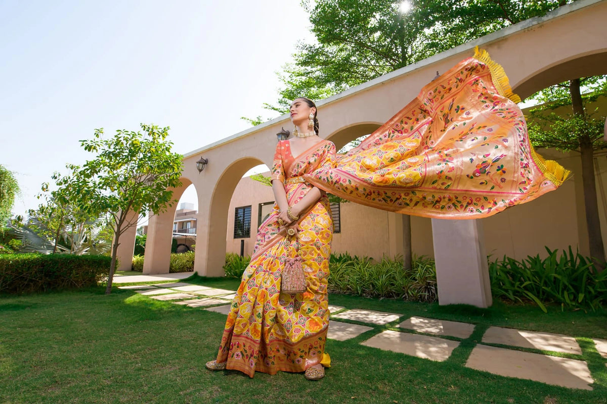 Woman in a colorful floral dress standing outdoors with a building and greenery in the background