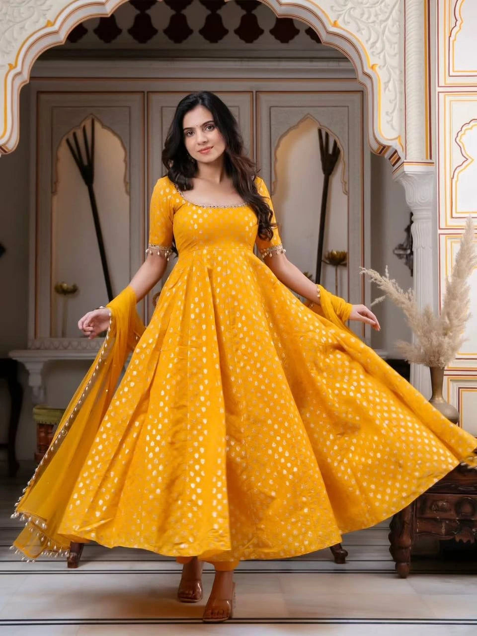 Woman in a yellow dress with white patterns standing in an ornate doorway.