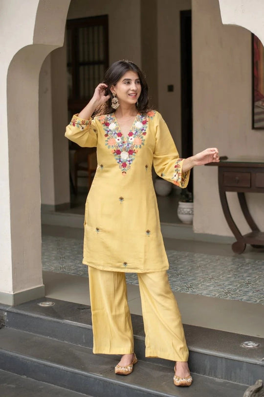 Woman in a yellow traditional outfit with floral embroidery standing on steps.