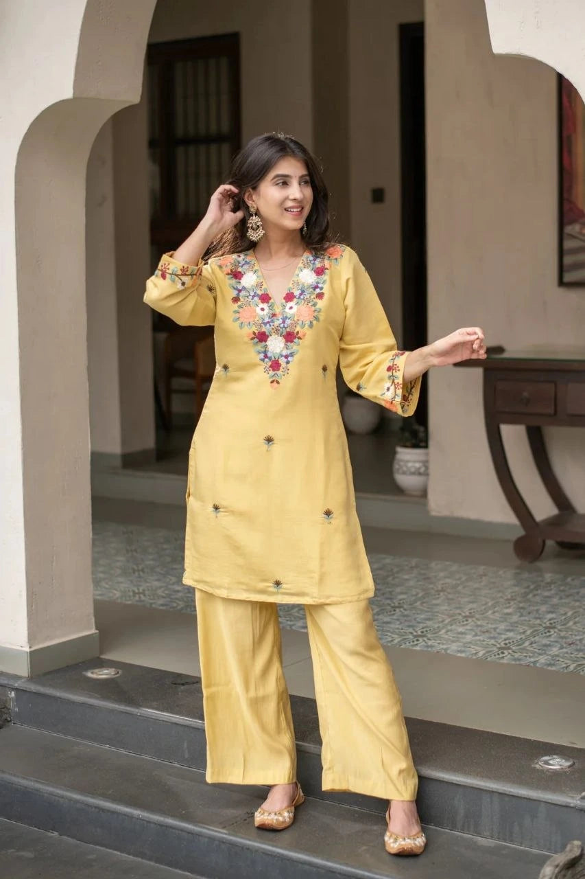 Woman in a yellow traditional outfit with floral embroidery standing on steps.