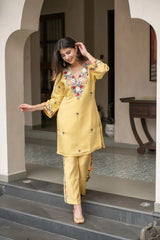 Woman in a yellow embroidered outfit standing on steps outside a building.