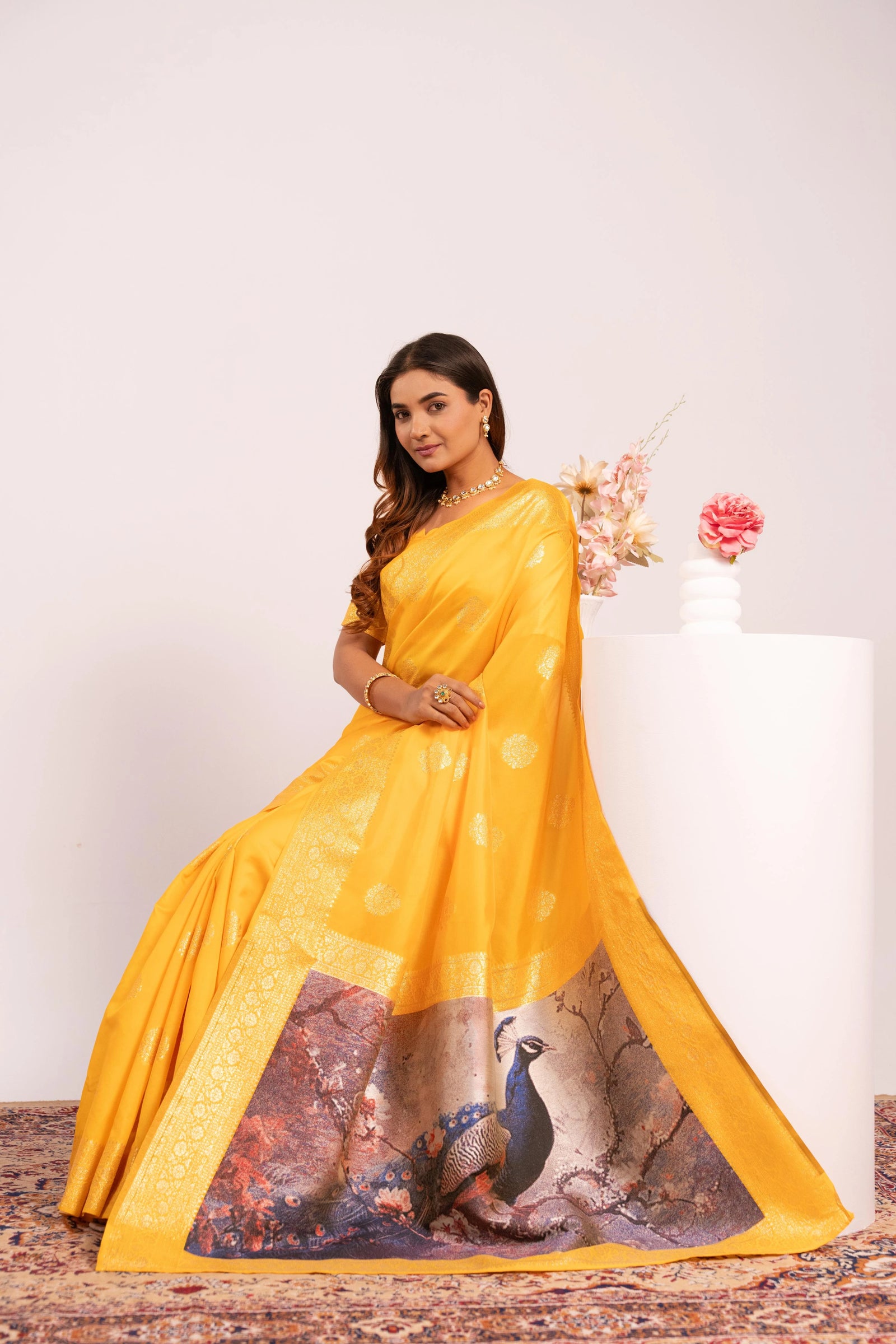 Woman wearing a yellow saree with a peacock design on a white background