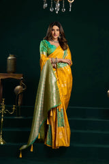 Woman in a yellow and green saree standing against a dark background