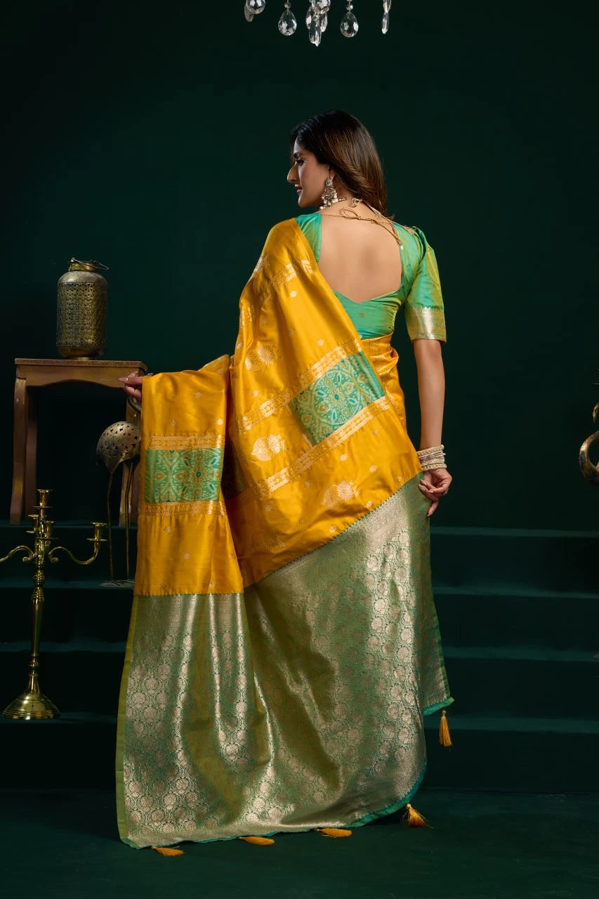 Woman in a yellow and green saree standing in a dimly lit room.