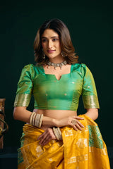 Woman wearing a green blouse and yellow saree with gold jewelry against a dark background
