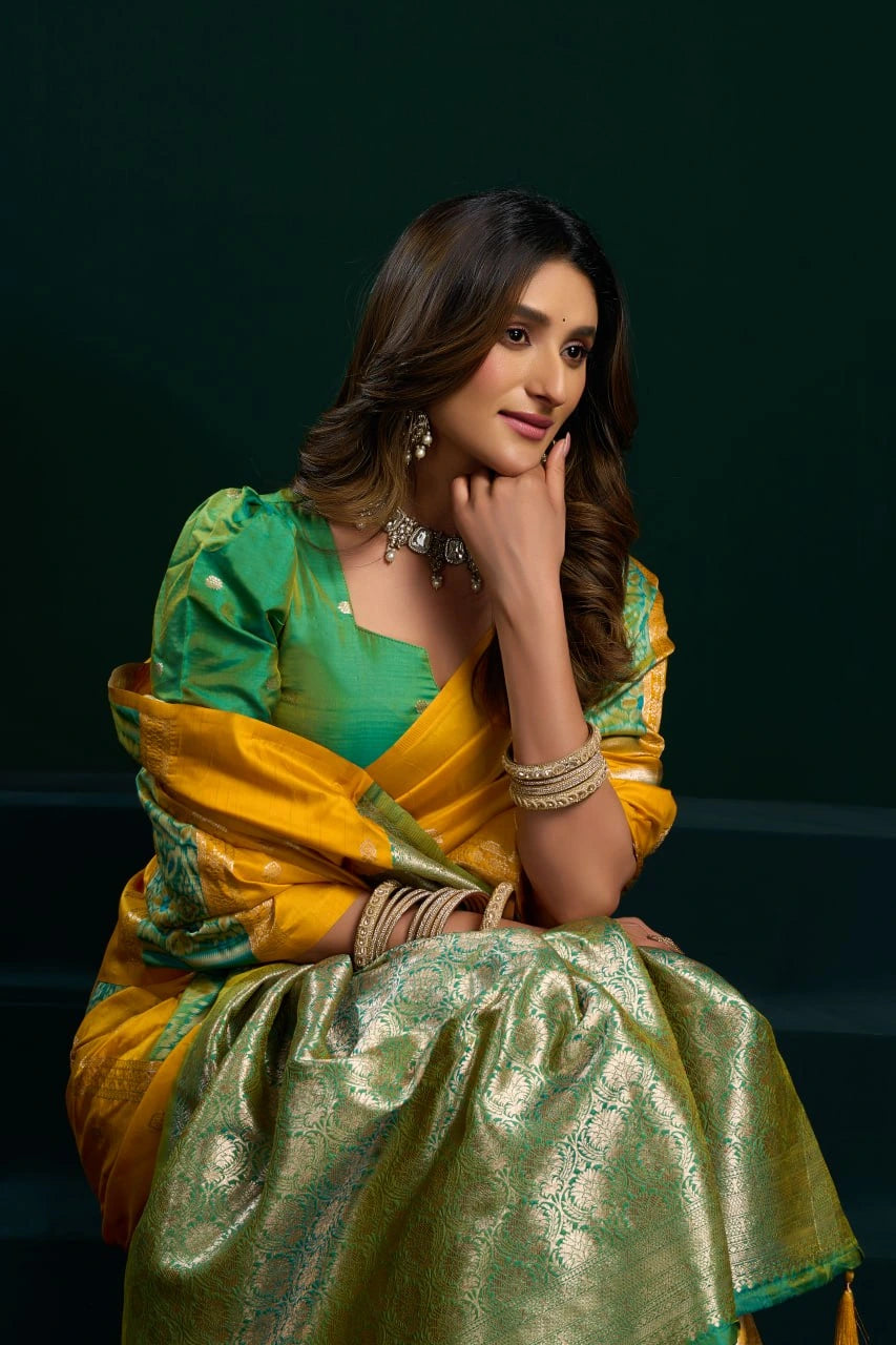 Woman in a green and yellow saree sitting against a dark background