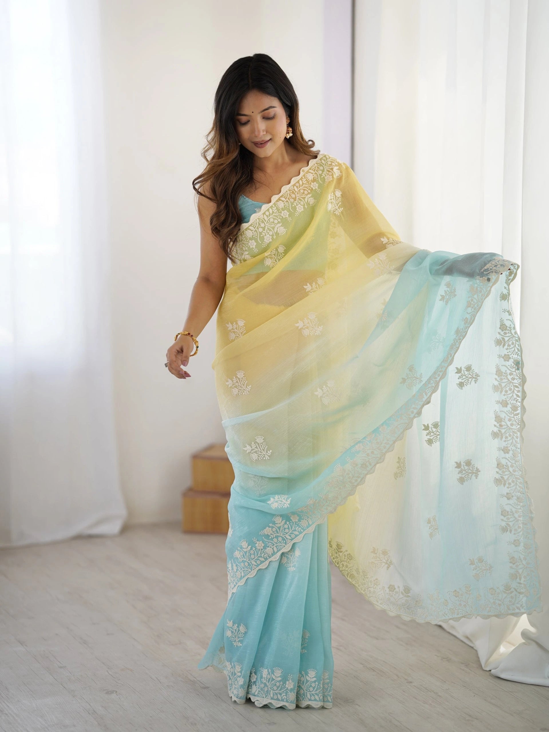 Woman wearing a light blue and yellow saree with white embroidery in a bright room.