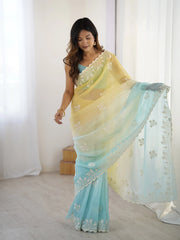 Woman wearing a light blue and yellow saree with white embroidery in a bright room.