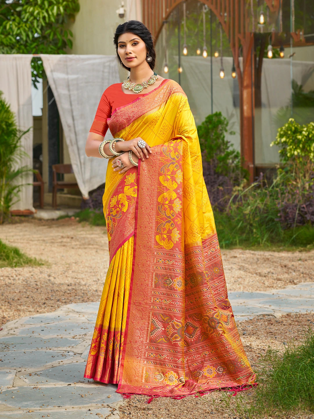 Woman wearing a yellow and red saree with a garden background