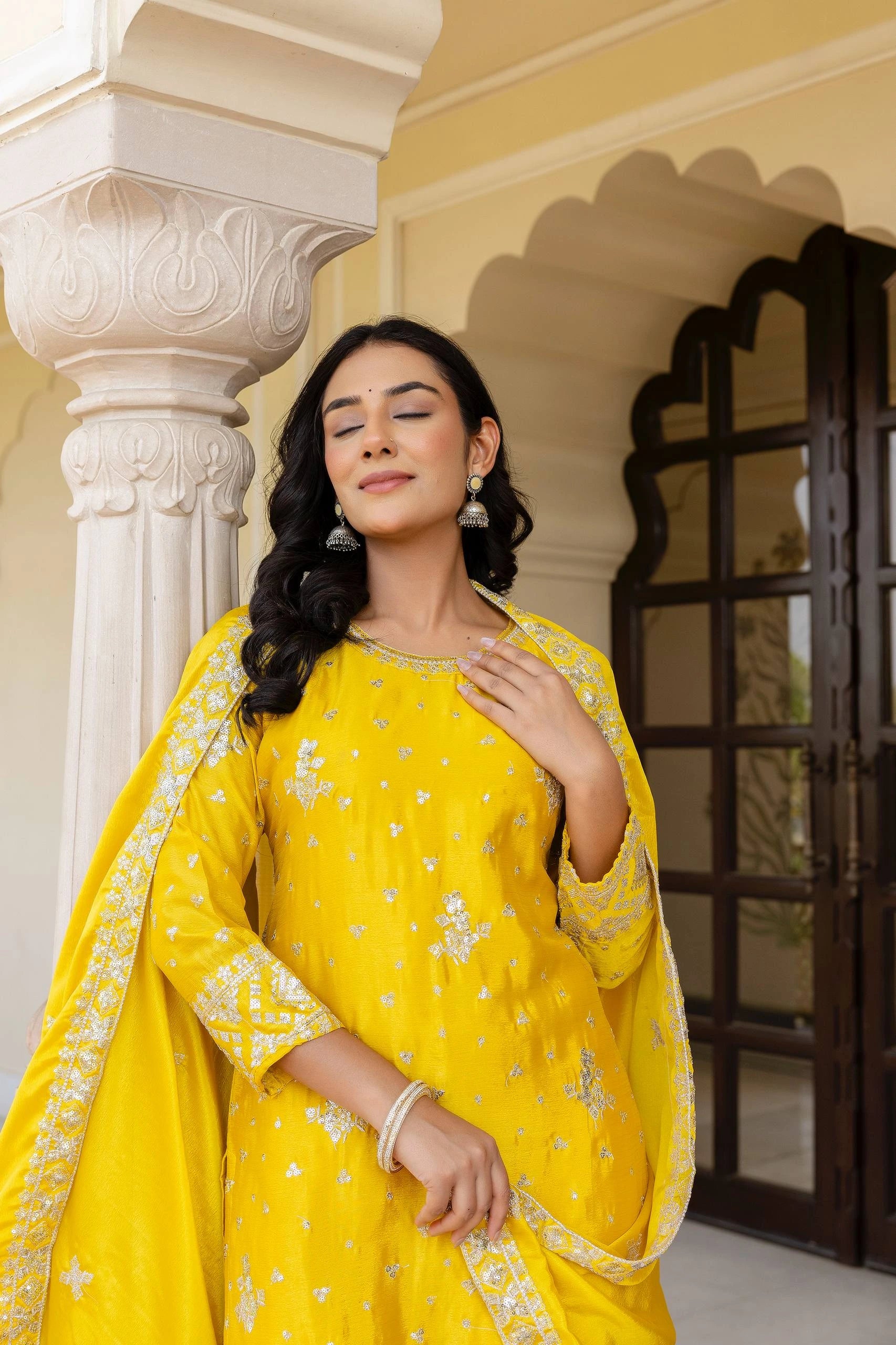 Woman in a yellow traditional outfit standing in front of a decorative building.