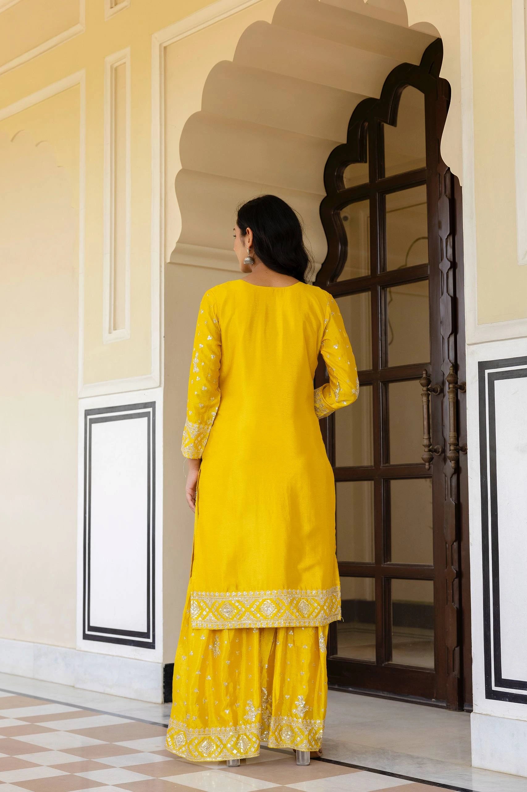 Woman in a yellow traditional outfit standing in a decorative doorway.