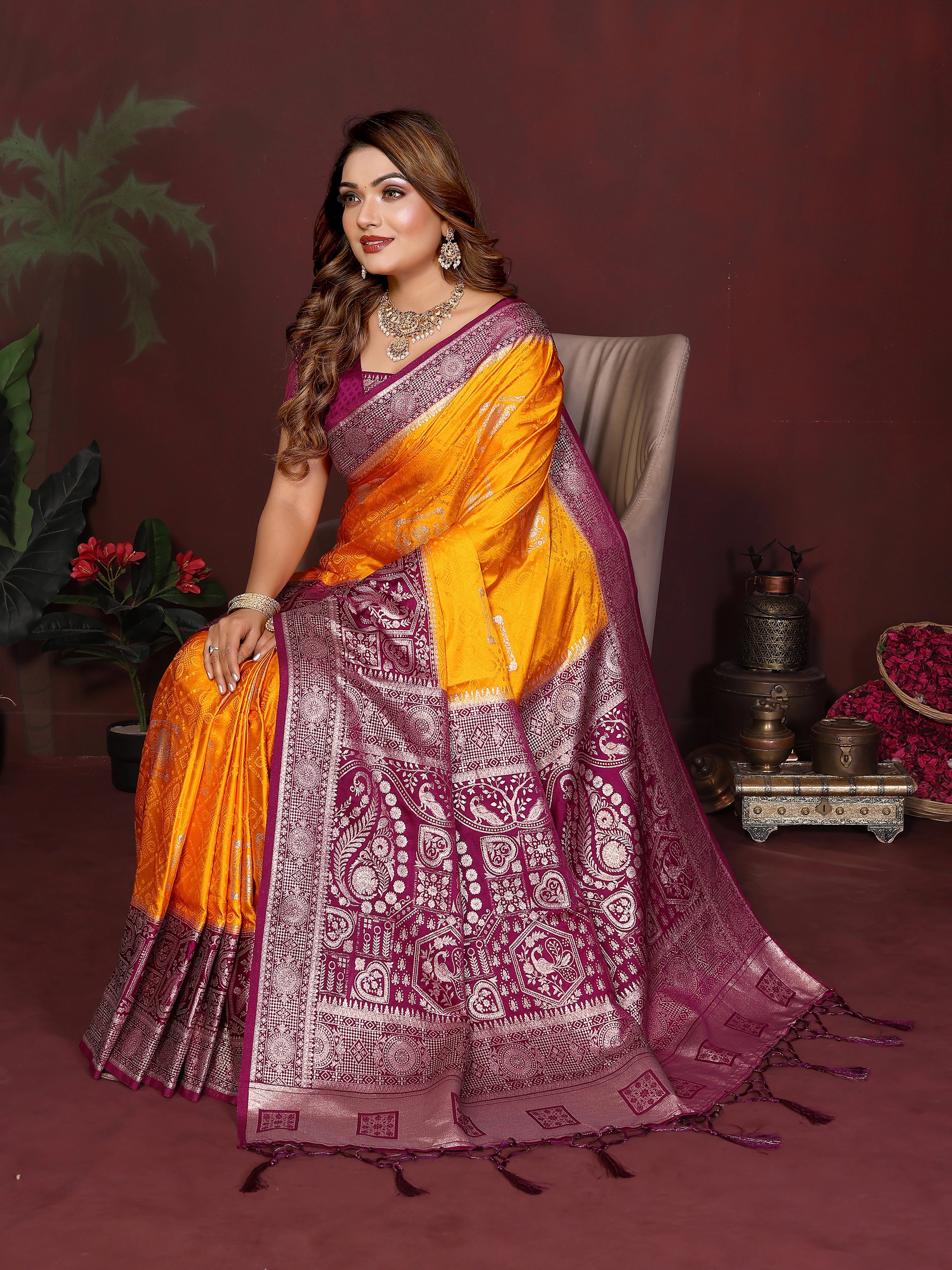 Woman in a traditional orange and purple saree sitting on a chair with a dark background