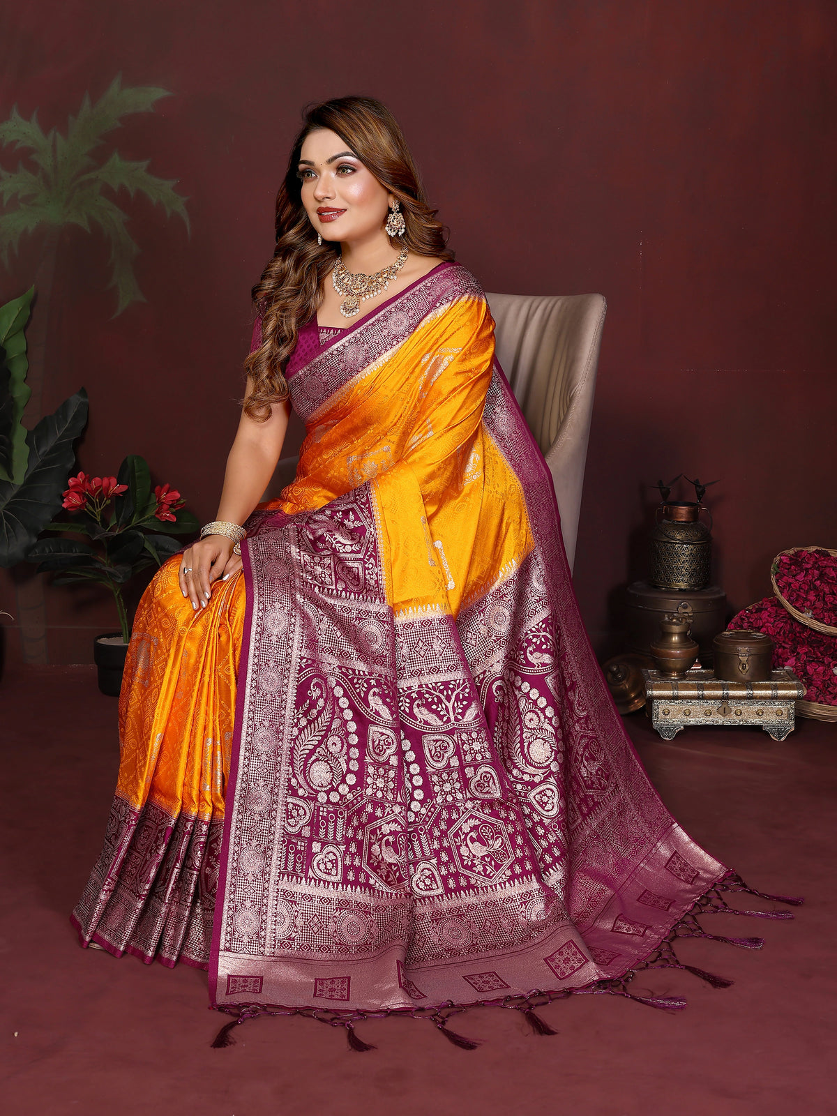 Woman in a traditional orange and purple saree sitting on a chair with a dark background