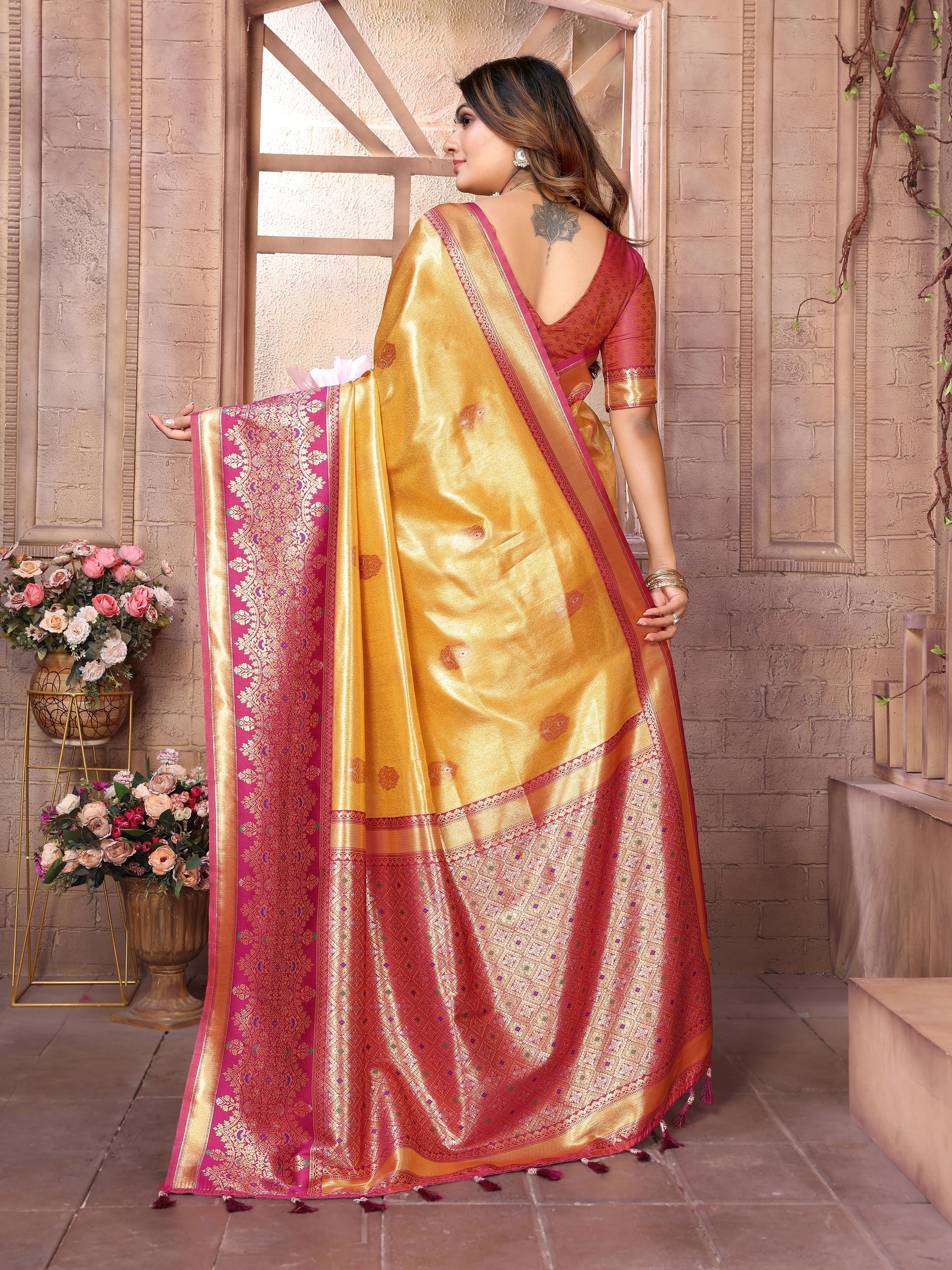 Woman wearing a yellow and red saree in an indoor setting with flowers and decor.