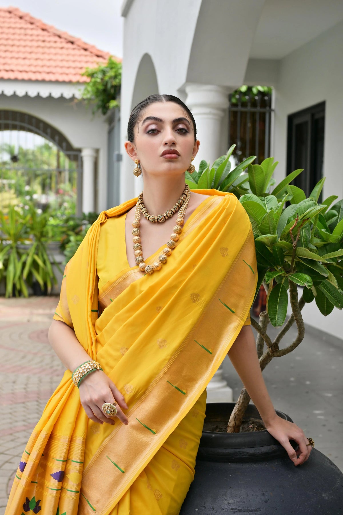 Woman in a yellow saree with a garden and building in the background