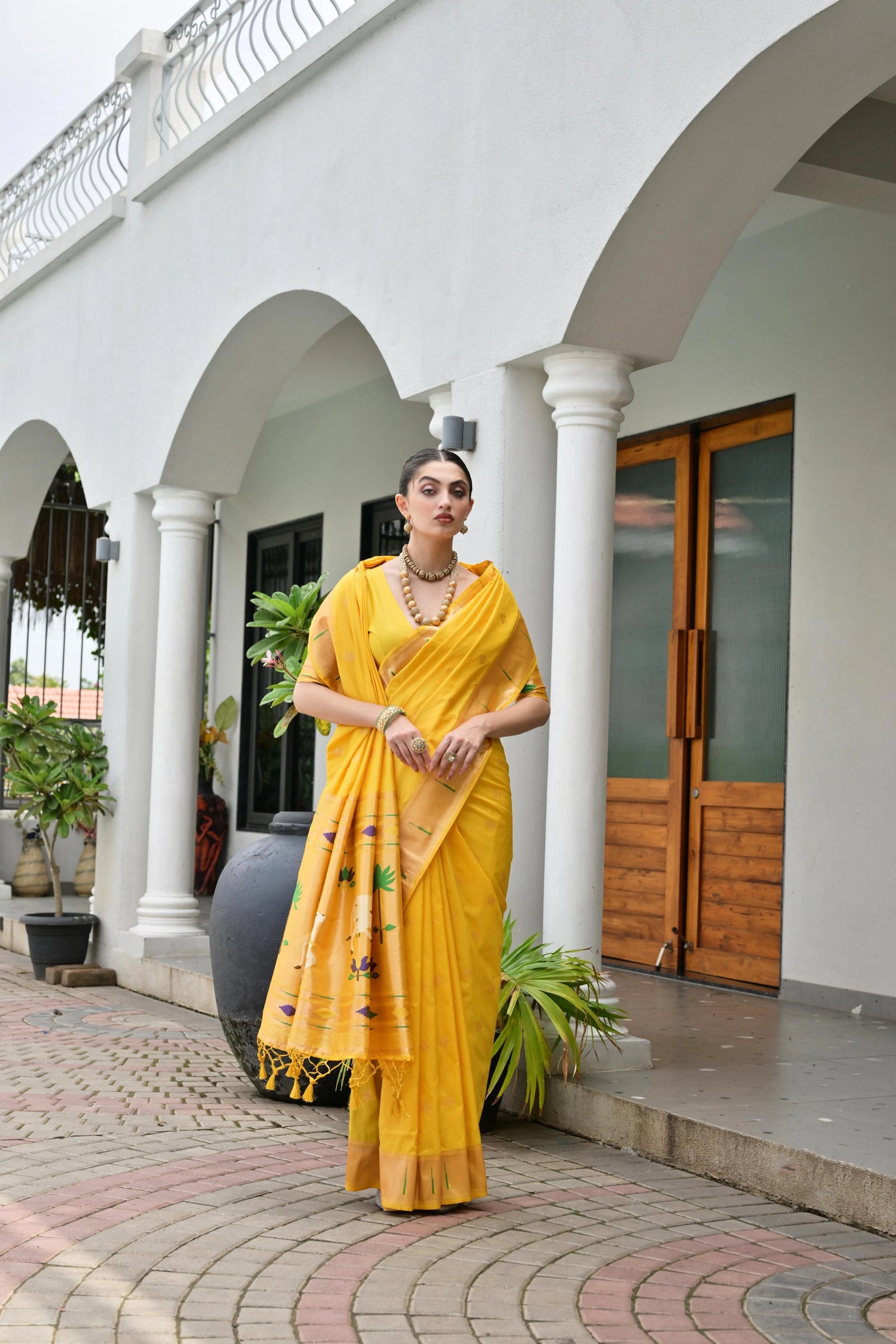 Woman in a yellow saree standing in front of a white building with columns.