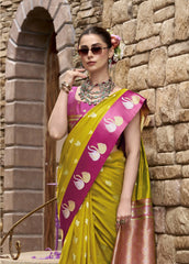 Woman in a yellow and pink saree standing against a stone wall.