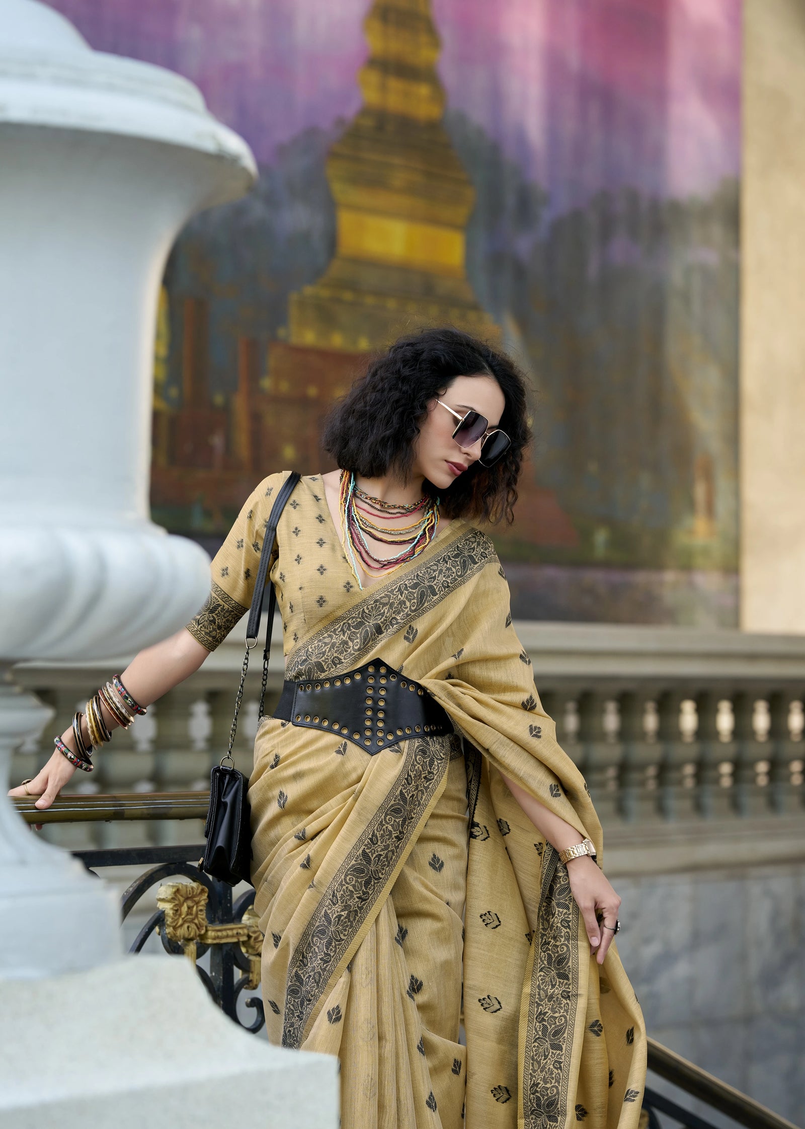 Woman in a beige saree with a decorative border standing in front of a colorful mural.