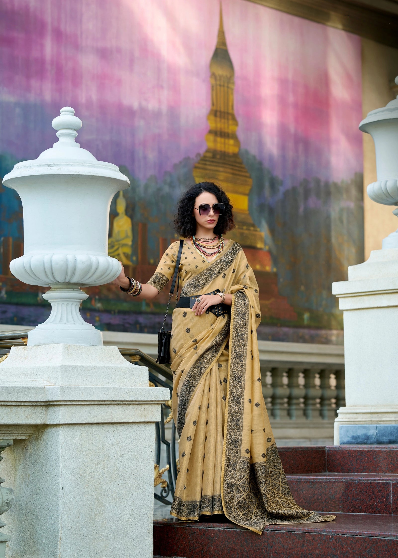 Woman in a beige saree standing on steps with a colorful mural in the background