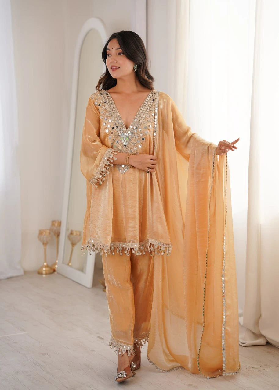 Woman wearing a peach-colored traditional outfit with intricate designs in a softly lit room.