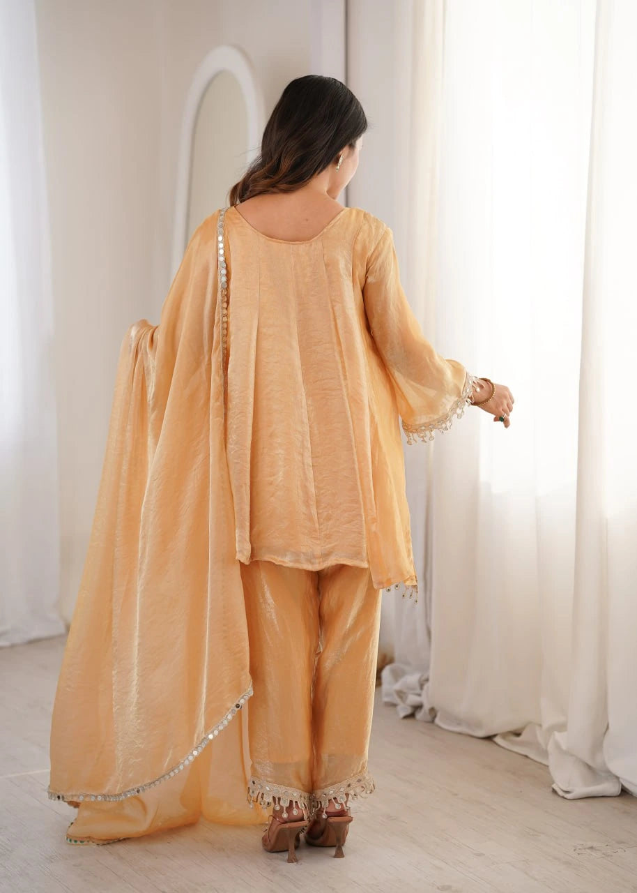 Woman in a peach traditional outfit standing in a bright room with white curtains.