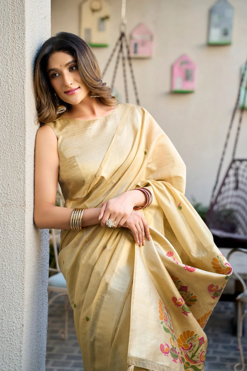 Woman in a light yellow saree with floral patterns, standing against a neutral wall.