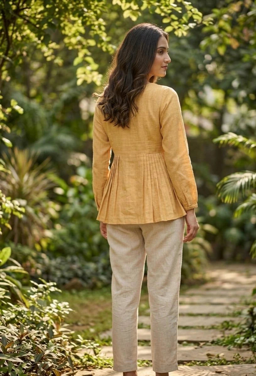 Woman wearing a mustard yellow jacket and beige pants standing in a garden.