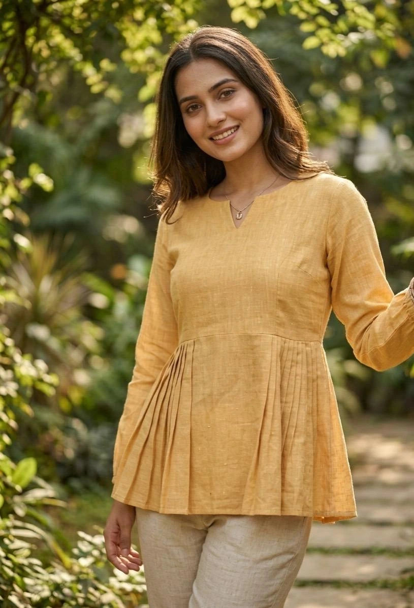 Woman wearing a yellow top and beige pants standing in a garden.
