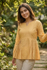 Woman wearing a yellow top and beige pants standing in a garden.