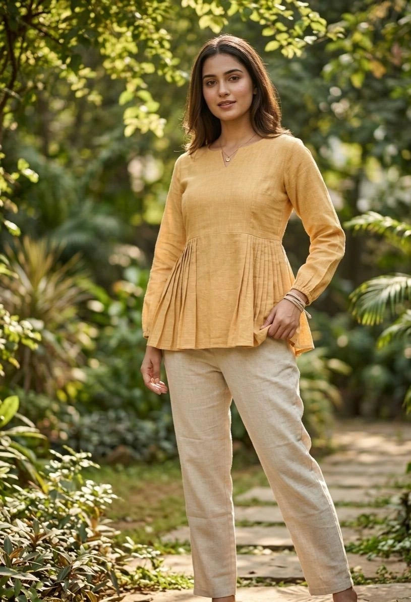 Woman wearing a mustard yellow top and beige pants standing in a garden.