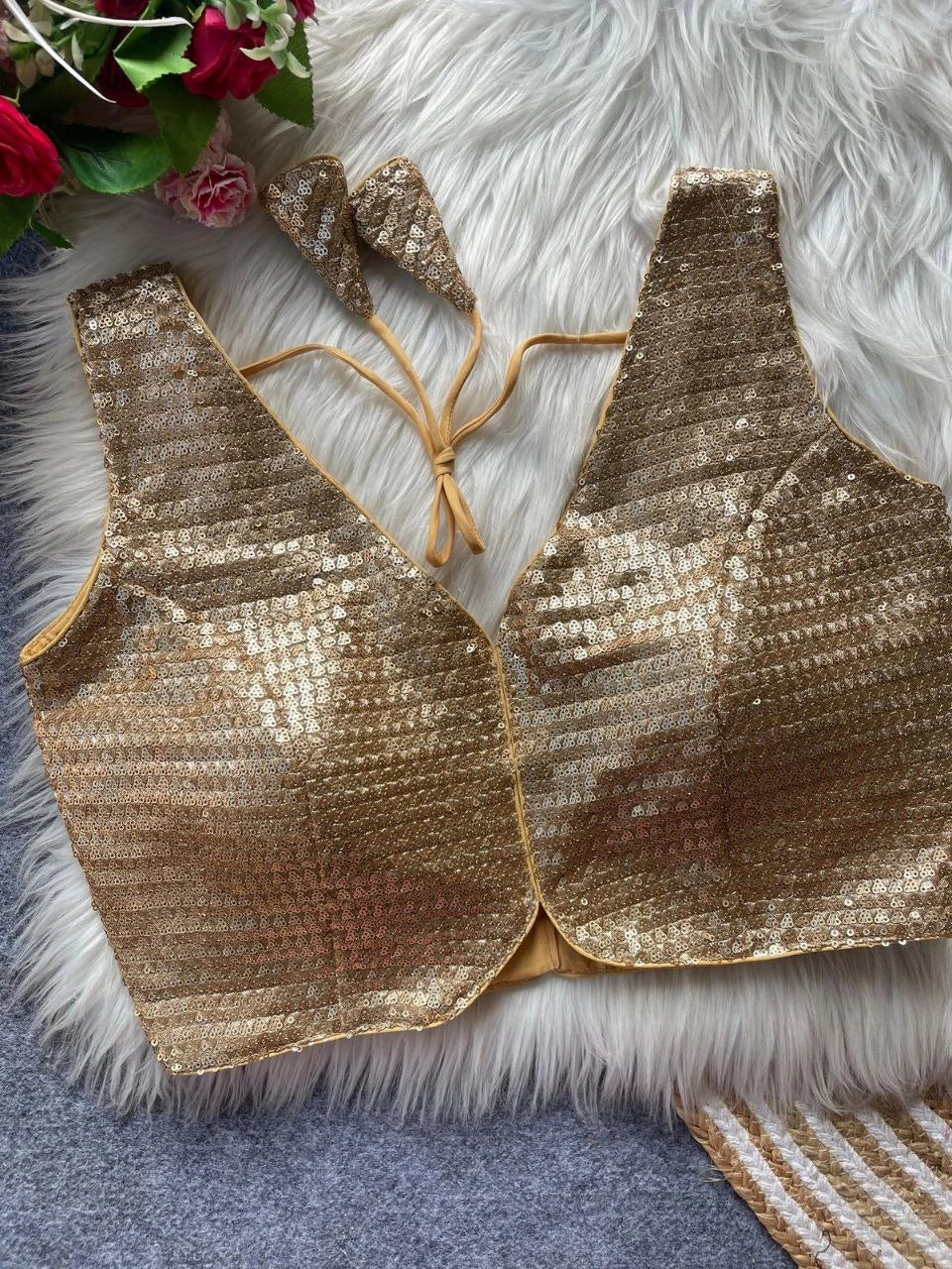 Gold sequin top on a textured surface with flowers in the corner