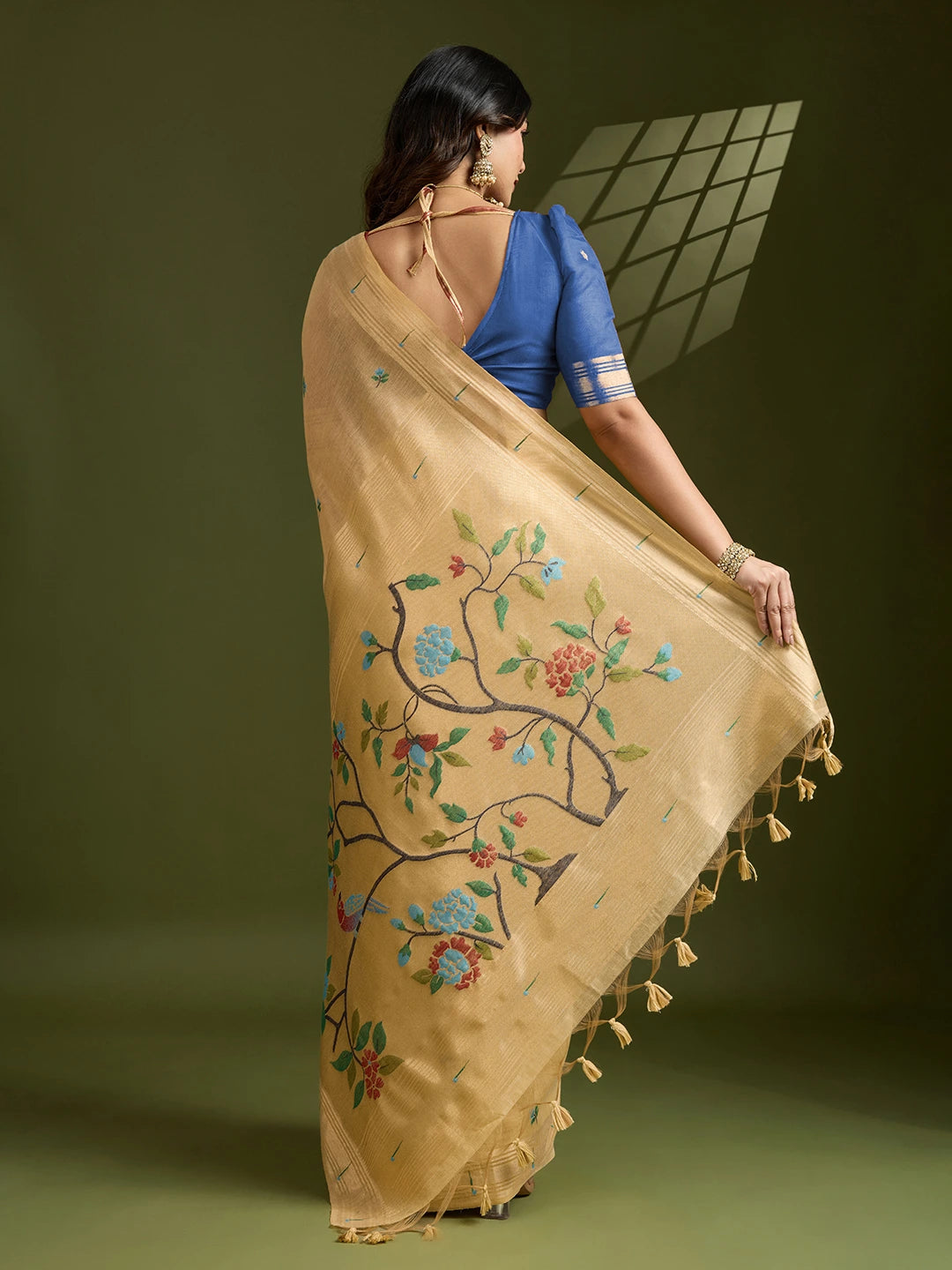Woman wearing a beige saree with floral embroidery and tassels on a green background