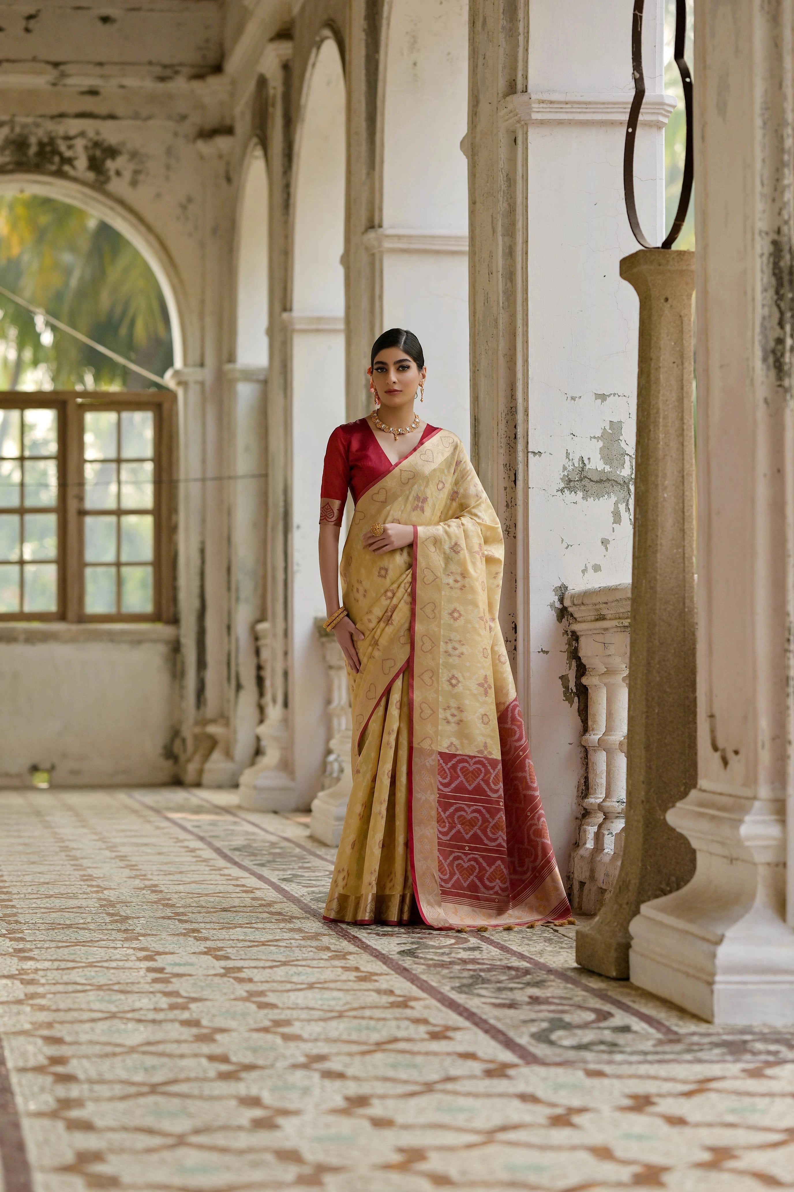 Woman in a traditional saree standing in an elegant indoor setting with architectural columns.