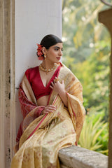 Woman in a traditional outfit with a red blouse and beige saree, standing in a garden.
