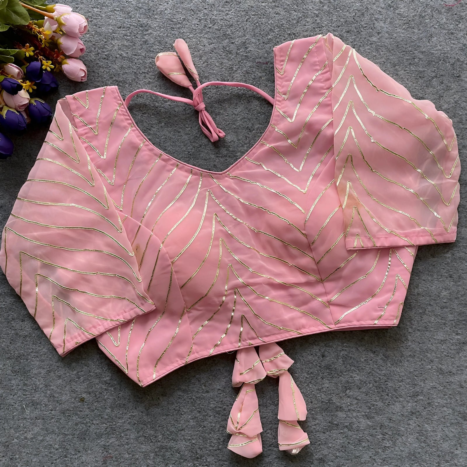 Baby pink georgette saree blouse featuring silver foil chevron embroidery, elbow-length sleeves, and back tie tassels for festive women’s wear.